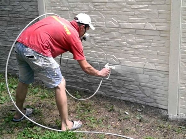 A man paints a fence with white paint